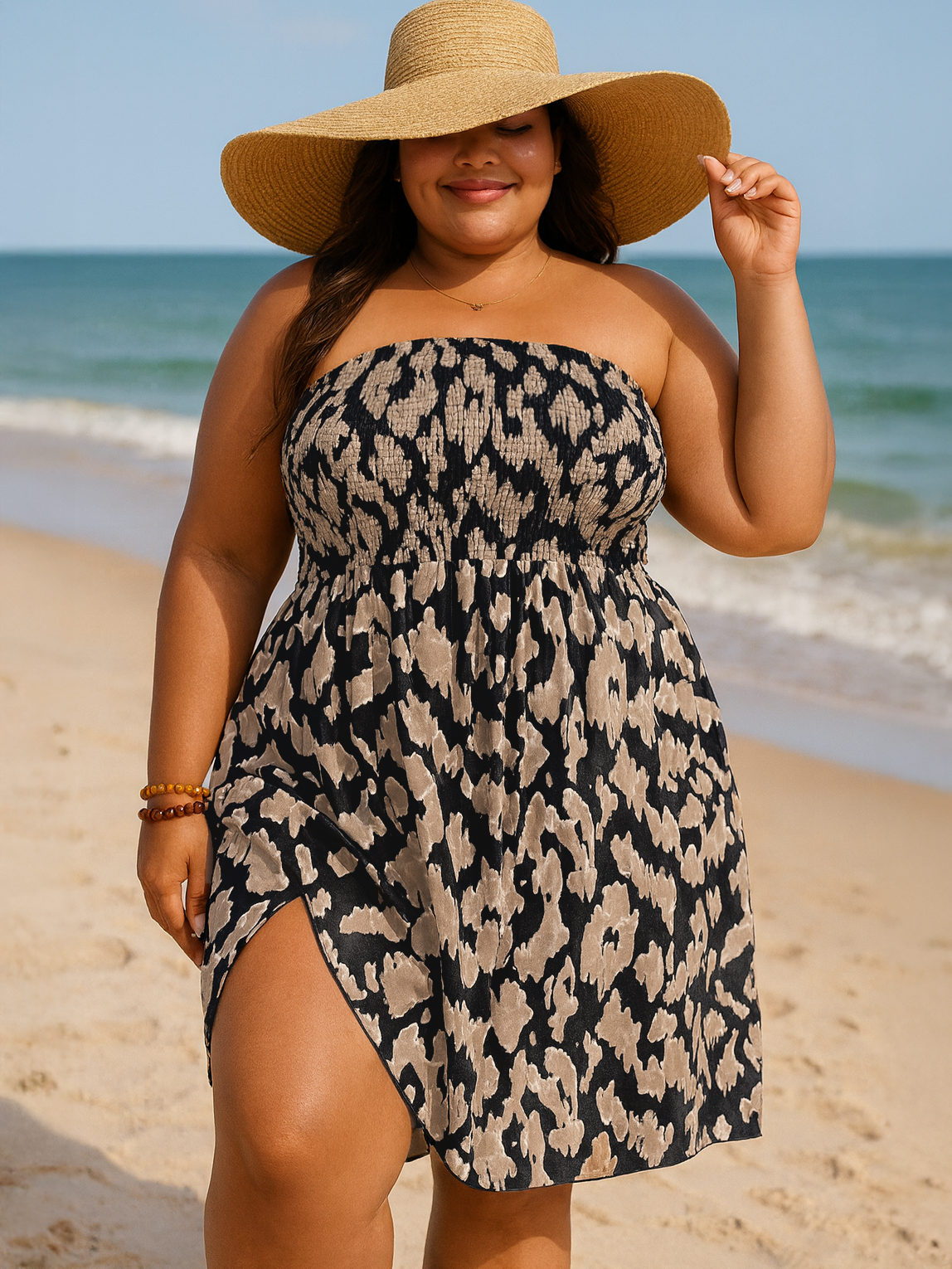 Woman in a strapless leopard print dress and wide-brimmed hat on a beach.