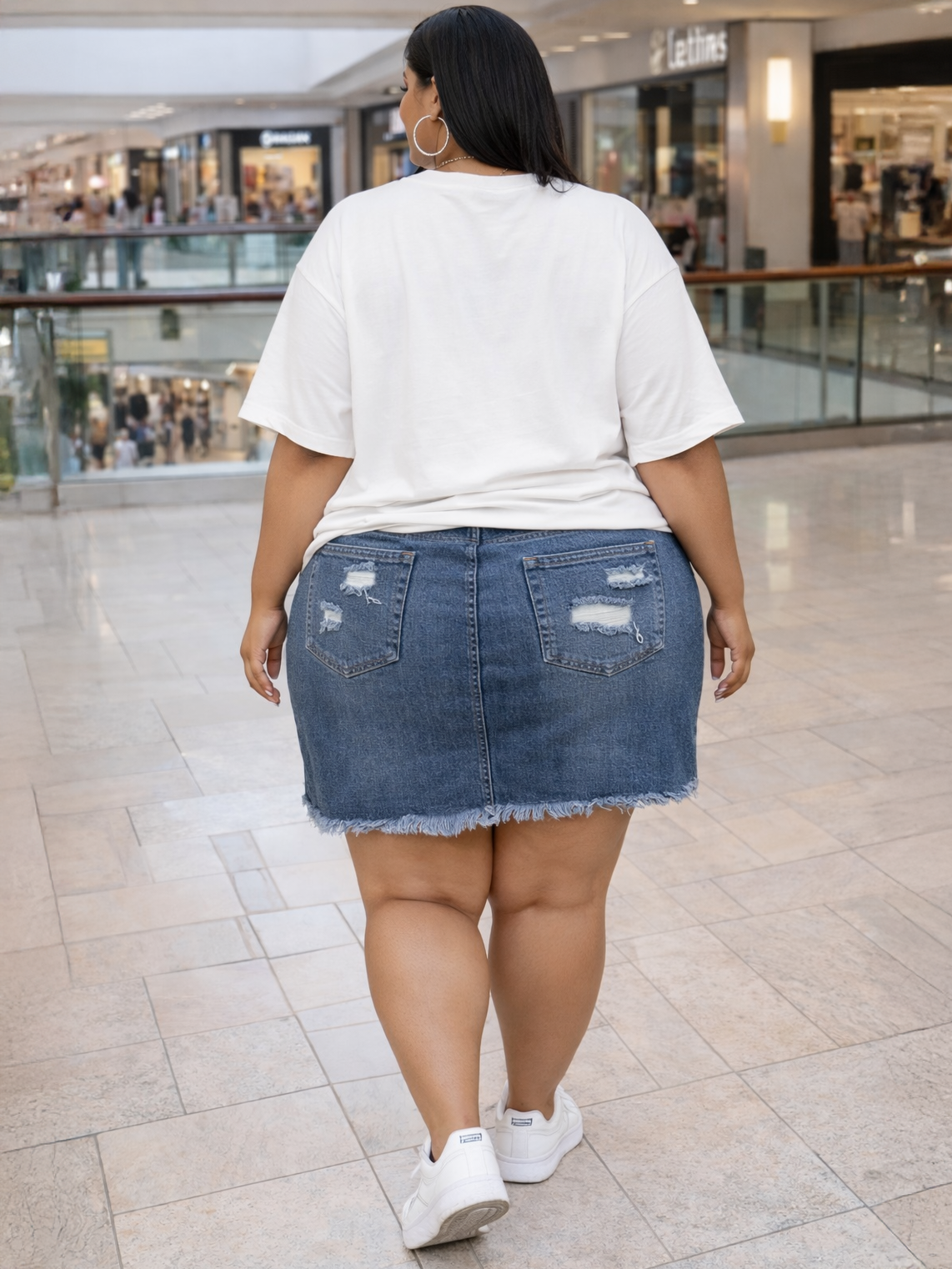 Person wearing a white t-shirt and denim skirt in a shopping mall.