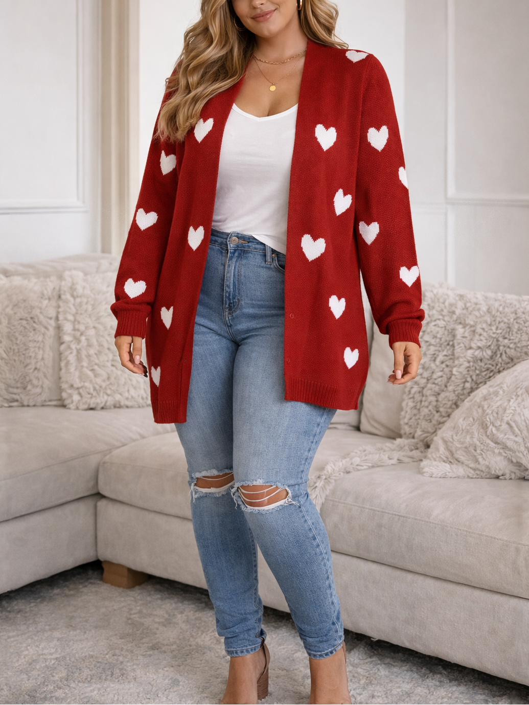 Woman wearing a red cardigan with white heart patterns, white top, and blue jeans in a living room.
