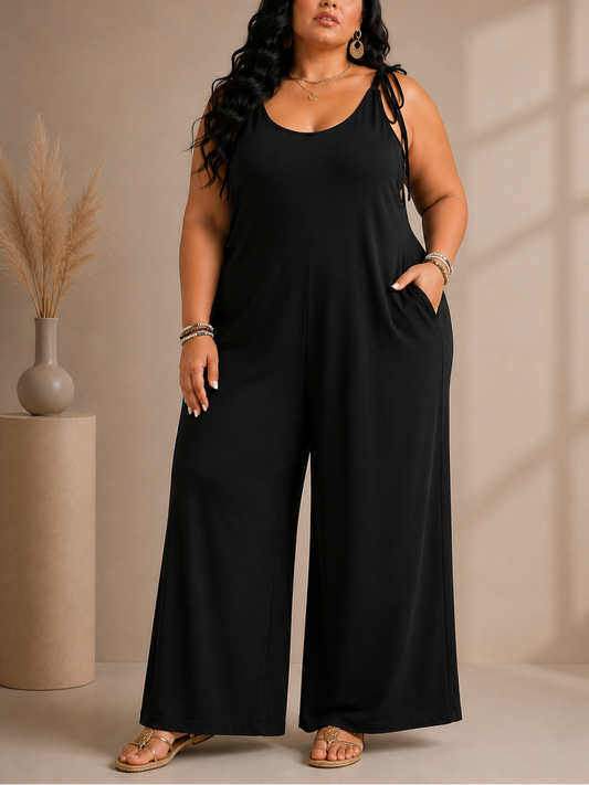 Woman wearing a black jumpsuit standing against a beige wall.