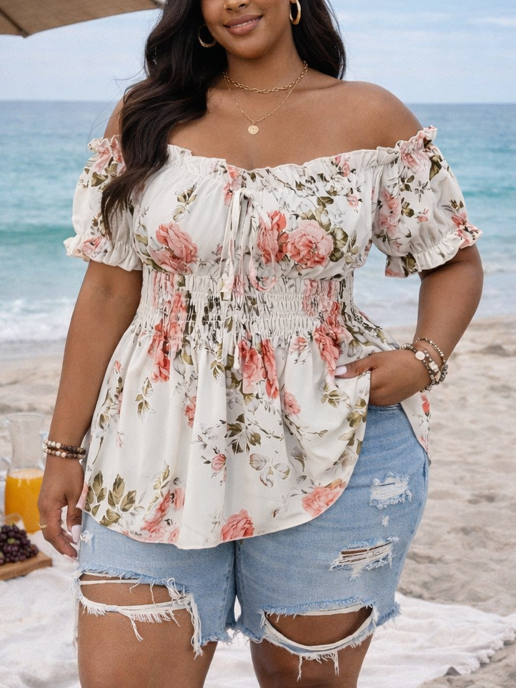 Woman in floral top and denim shorts standing on a beach with ocean view