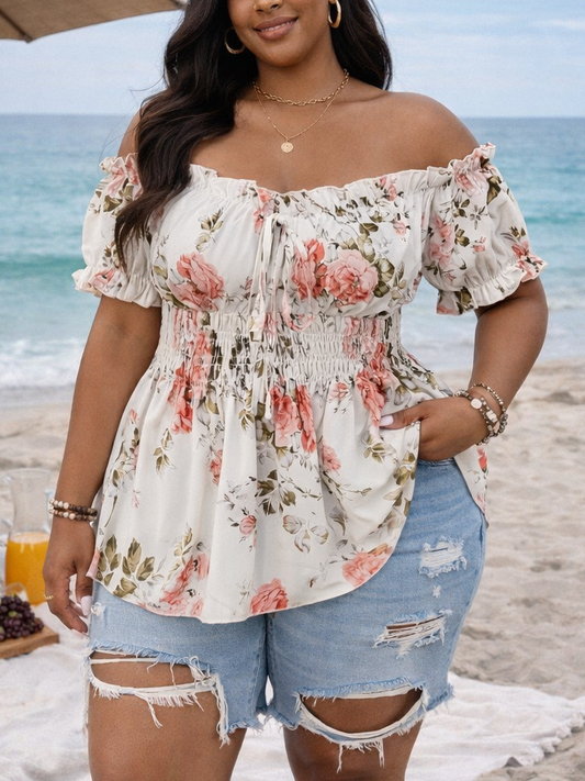 Woman in floral top and denim shorts standing on a beach with ocean view