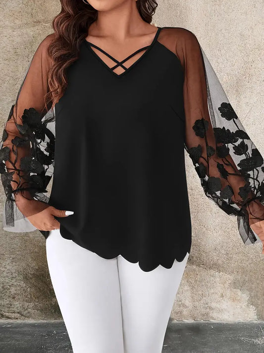Black top with sheer sleeves and floral embroidery worn by a plus size woman against a neutral background