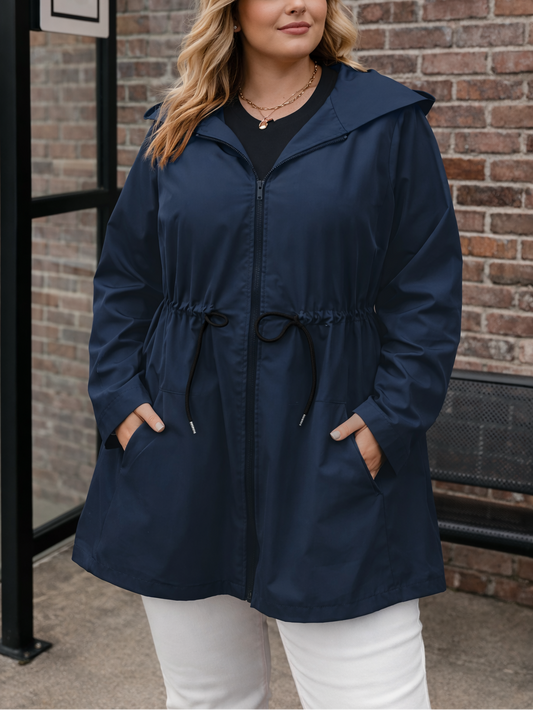 Woman wearing a navy blue raincoat standing against a brick wall.