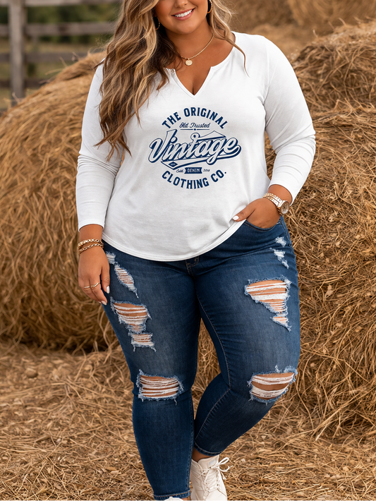 Woman wearing a white long-sleeve shirt with text and blue jeans standing in front of hay bales.